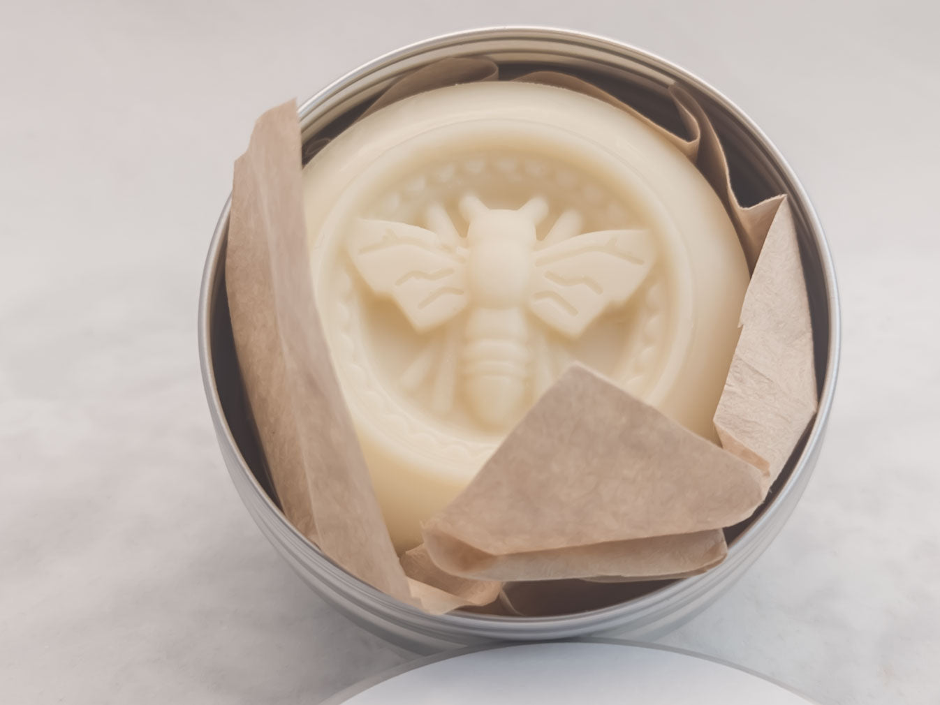 Shimmering Strawberry lotion bar in a silver tin with the lid off on white background. Luxurious skin nourishing lotion bar. Romantic scent.