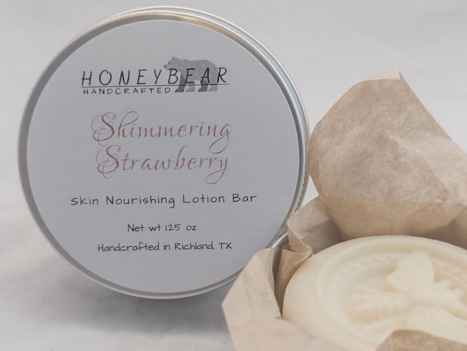 Shimmering Strawberry lotion bar in a silver tin on white background. Luxurious skin nourishing lotion bar. Romantic scent. With open lotion bar near the side of the labeled lotion bar